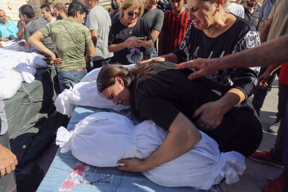 A Palestinian woman mourns over the bodies of her relatives who were killed in Israeli airstrikes that hit a Greek Orthodox church, during their funeral in Gaza City. 20 October 2023. (Alamy)